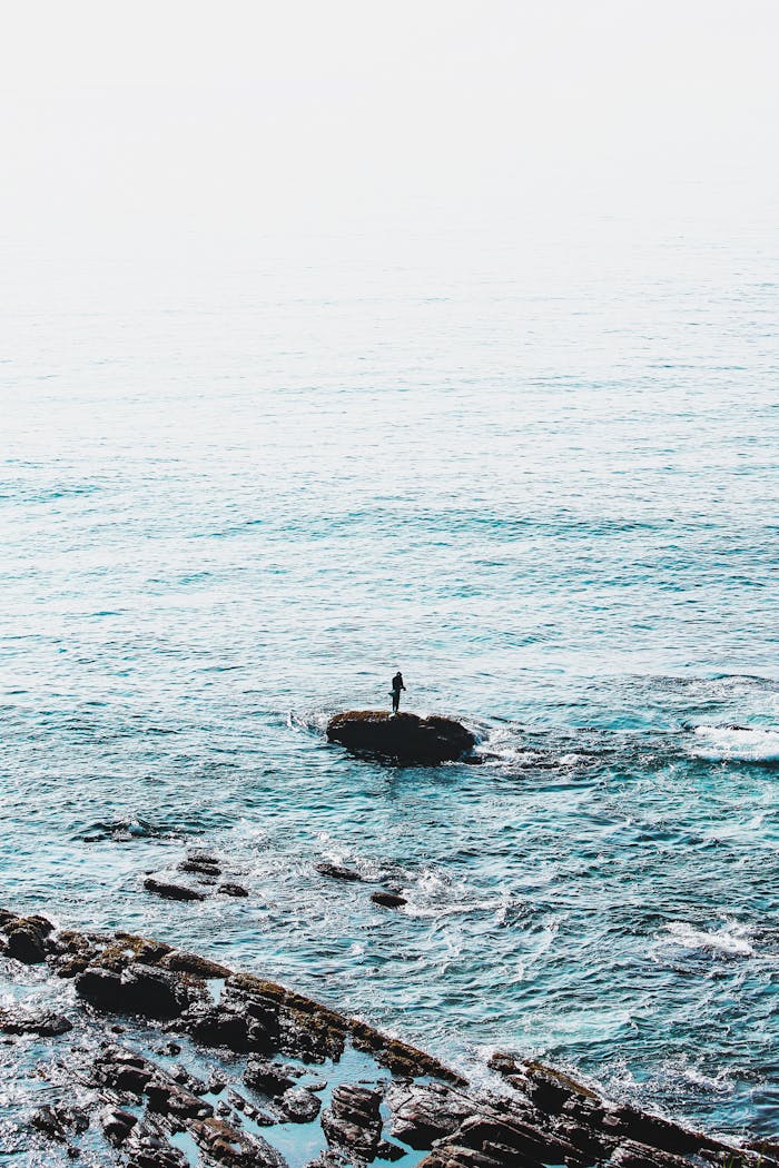 A lone person stands on a rock by the serene ocean waves in Dambulla, Sri Lanka.